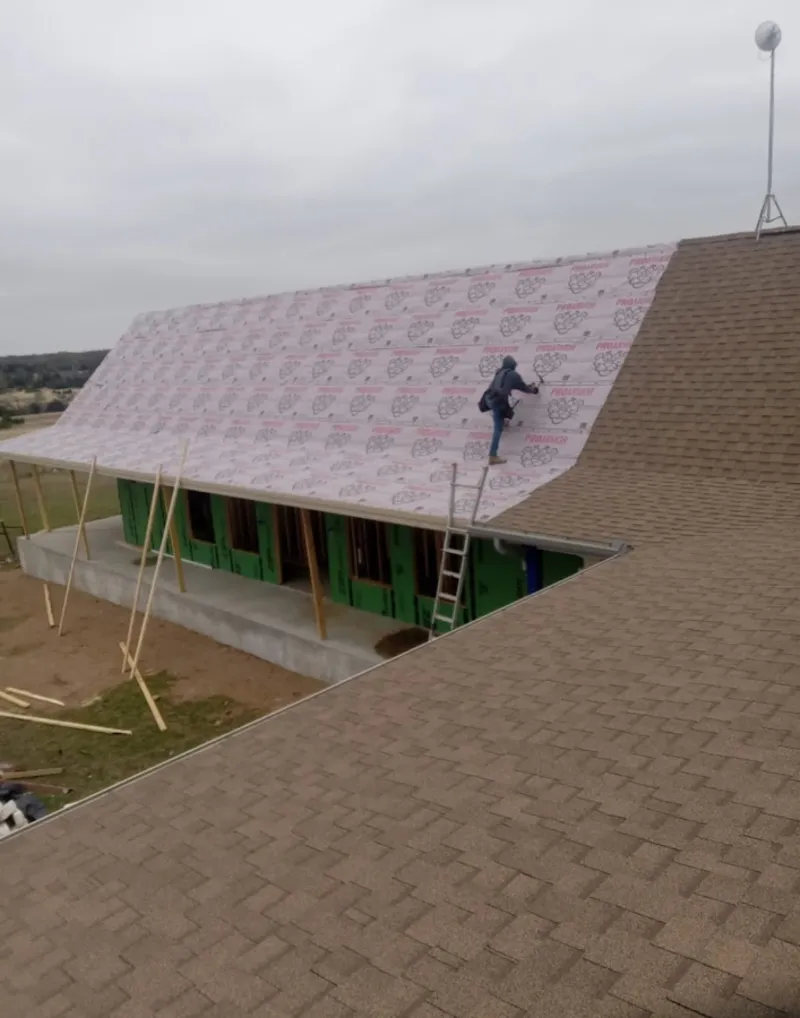 Worker preparing underlayment for a metal roof installation in Cuero